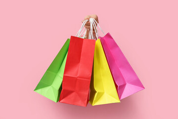 Female hand with colorful shopping bags visible through hole on torn pink background
