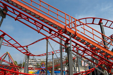 Bright red roller coaster tracks with steel supports against a blue sky in an amusement park setting