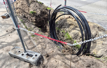 Trench with coiled black cables, secured by red and white chains, indicating ongoing repair or new...
