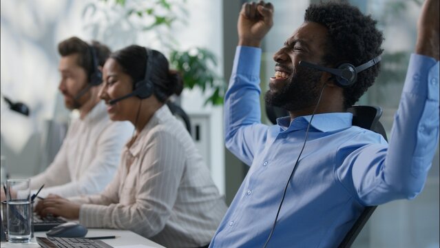 Happy excited multiethnic coworkers African and Caucasian men business call center operators celebrate victory win promotion triumph shout joy assistant headset Indian woman work success in callcenter