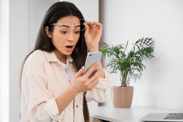Shocked young woman using mobile phone at home