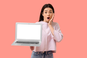 Shocked young woman with blank laptop on pink background