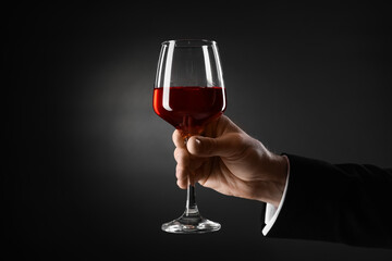 Businessman holding glass of wine on black background