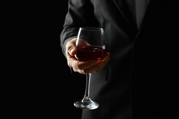 Businessman holding glass of wine on black background