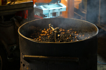 Metal drum-style roasting machine in action, filled with chestnuts and black sand or gravel