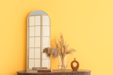 Mirror and pampas grass on chest of drawers near yellow wall in room, closeup