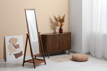 Big floor mirror and chest of drawers near beige wall in interior of room
