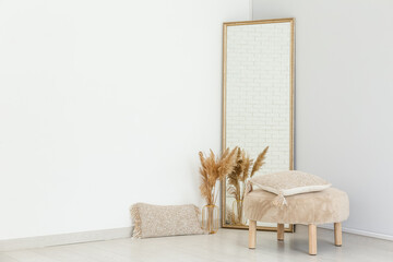 Floor mirror, pouf and vase with pampas grass near white wall in room