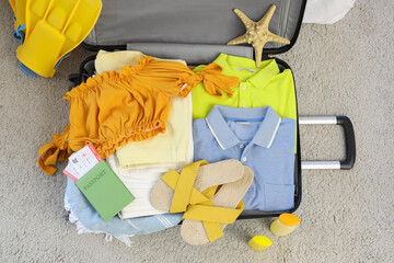 Packed suitcase with clothes and beach accessories on carpet in room, closeup