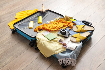Packed suitcase with photo camera, clothes and accessories on floor in room, closeup