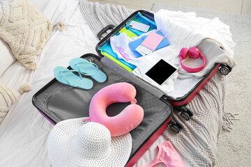 Open suitcase with headphones, clothes and accessories on bed in bedroom, closeup