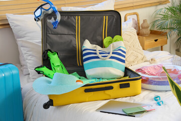 Open suitcase, laptop and beach accessories on bed in bedroom, closeup