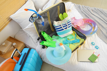 Open suitcase, laptop and beach accessories on bed in bedroom