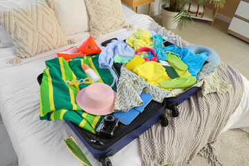 Packed suitcase with clothes and beach accessories on bed in bedroom, closeup