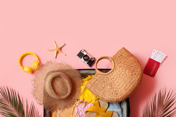 Packed suitcase with clothes and beach accessories on pink background, closeup