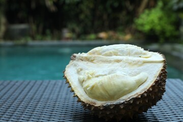 Fresh ripe durian on wicker table near swimming pool outdoors, closeup. Space for text