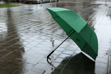 Green umbrella on wet asphalt outdoors, space for text