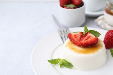 Tasty panna cotta with caramel, strawberries and mint on light table, closeup. Space for text