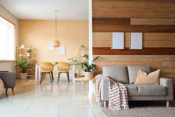Interior of light living room with table, sofa and houseplant near wooden wall