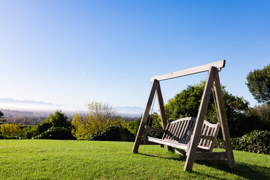 Fototapeta Wooden swing bench resting on neatly mowed lawn atop sloping hill, overlooking distant valley