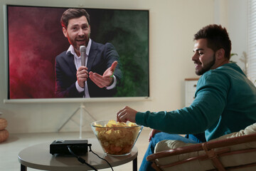 Young man watching entertainment show using video projector at home