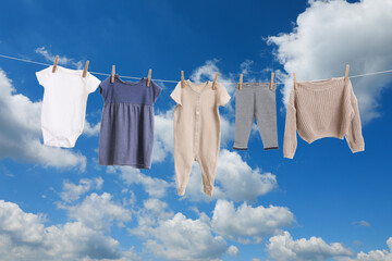 Different baby clothes drying on washing line against blue sky