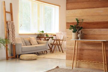 Interior of light living room with grey sofa, table and stepladder near window