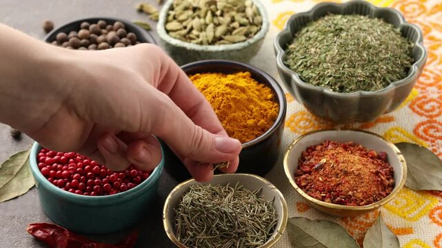 Woman with many different aromatic spices in bowls at grey table with cloth, closeup
