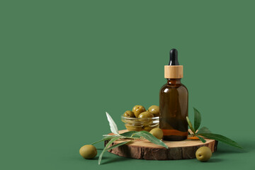 Composition with wood round slice and bottle of essential olive oil on green background
