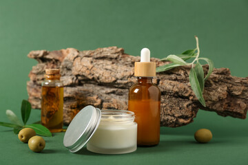 Composition with tree bark, bottles of essential olive oil and jar of cosmetic product on green...