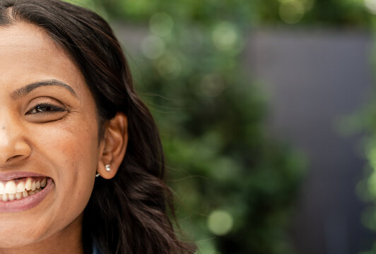 Indian woman smiling in backyard showing silver stud earrings and denim shirt collar, copy space
