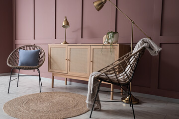Chest of drawers, armchairs and floor lamp near brown wall in interior of living room