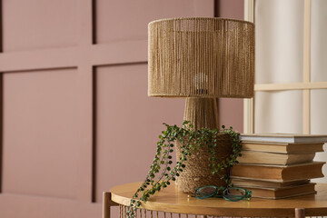Lamp, books and houseplant on table near brown wall in living room, closeup