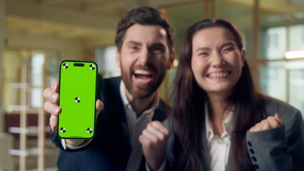 Excited two business woman man celebrating win showing mobile phone green screen chroma key mock up Caucasian Korean businesspeople cheering winner victory money smartphone excitement triumph office