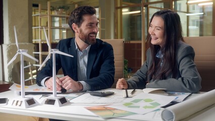 Happy joy Caucasian businessman Korean businesswoman discuss wind turbine model pointing finger...