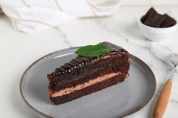 Plate with piece of tasty chocolate cake and mint leaf on marble background, closeup