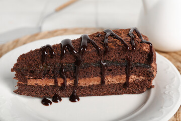 Plate with piece of tasty chocolate cake on wicker mat, closeup
