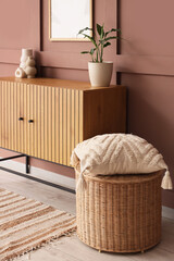 Chest of drawers, table and pouf near brown wall in interior of living room, closeup