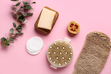 Composition with massage body brush, glove, soap bar and green twig on pink background, closeup