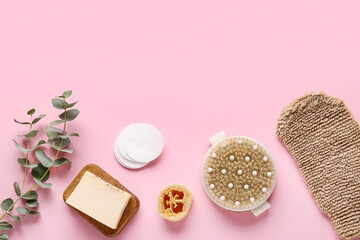 Composition with massage body brush, glove, soap bar and green twig on pink background, closeup