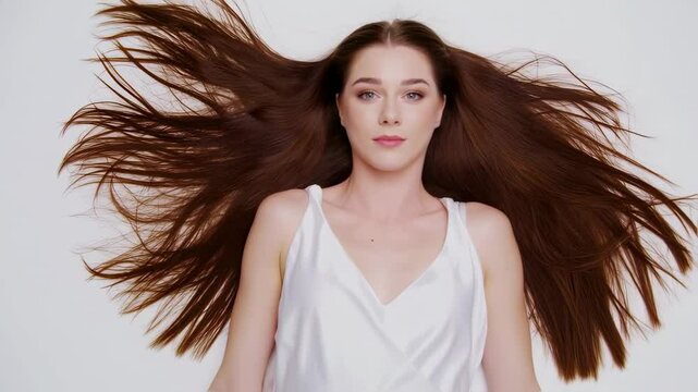 Beautiful woman with long brown hair flailing around in a studio, hair care commercial