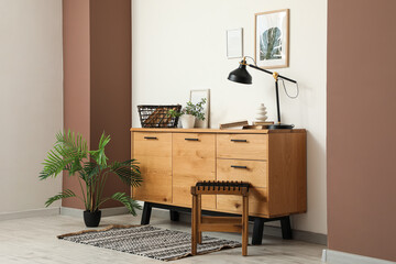 Interior of living room with chest of drawers, stool and houseplant near white wall