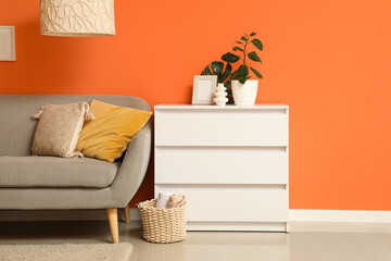 Chest of drawers, pouf and sofa near orange wall in interior of living room, closeup
