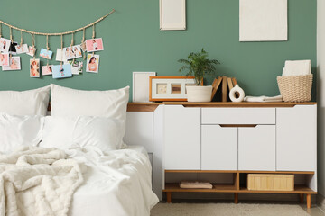 Interior of bedroom with big comfortable bed and chest of drawers near green wall, closeup