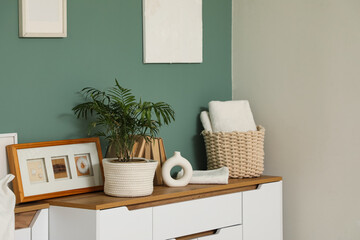 Vase, houseplant and photo frames on chest of drawers near green wall in bedroom, closeup