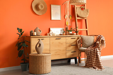 Chest of drawers, stepladder, armchair and table near orange wall in interior of living room