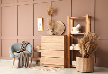 Chest of drawers, shelving unit and armchair near brown wall in interior of living room
