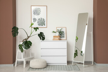 Interior of living room with chest of drawers, floor mirror and pouf near white wall