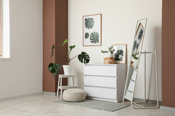 Interior of living room with chest of drawers, floor mirror and pouf near white wall