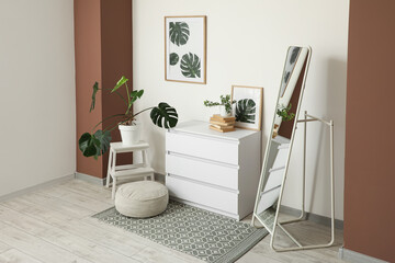 Interior of living room with chest of drawers, floor mirror and pouf near white wall